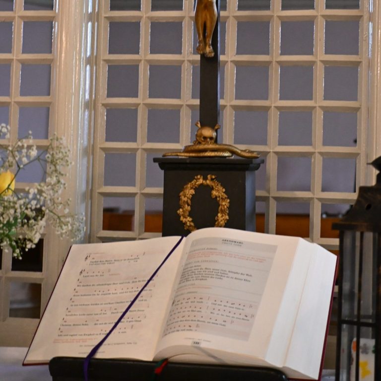 Ein offenes Buch mit Noten, hinter dem eine Statue und Blumen dekoriert sind.