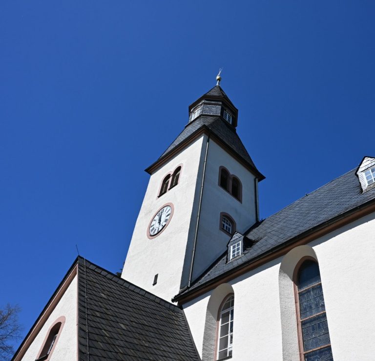 Weißer Kirchturm mit Uhr unter klarem blauen Himmel.