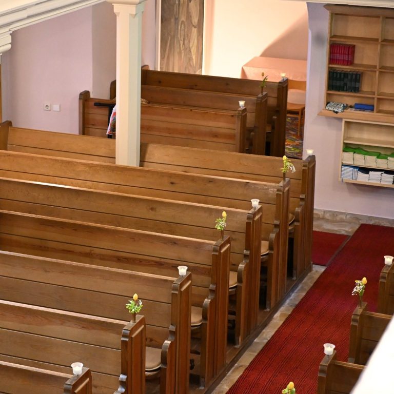 Holzbänke in einer Kirche mit roten Teppichen und Bücherregal an der Wand.