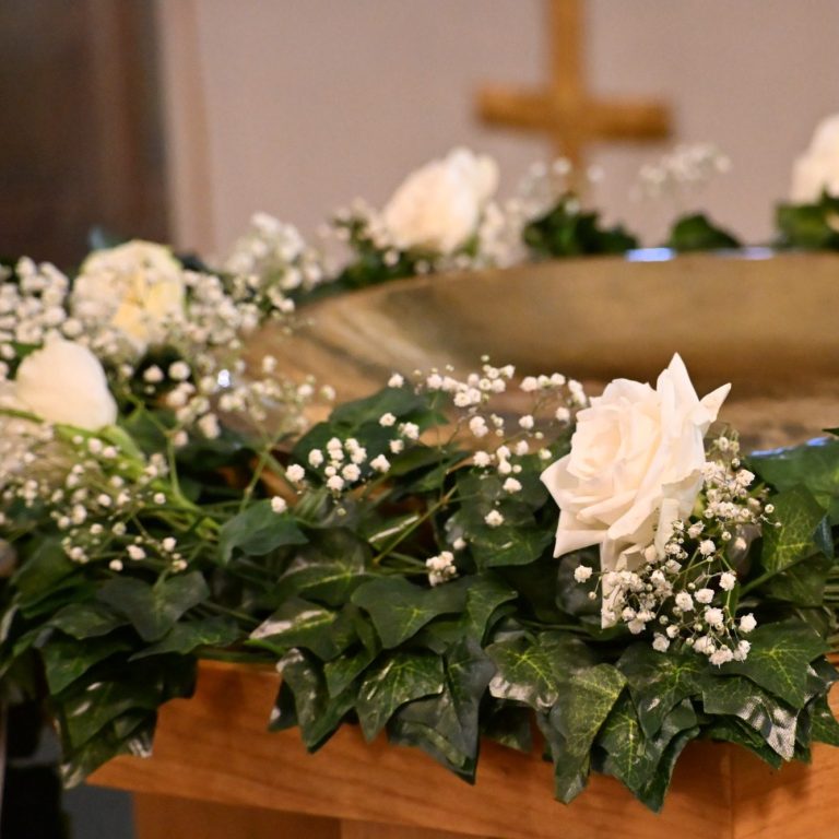 Ein goldener Taufbeckenrand, geschmückt mit weißen Rosen und grünem Efeu.