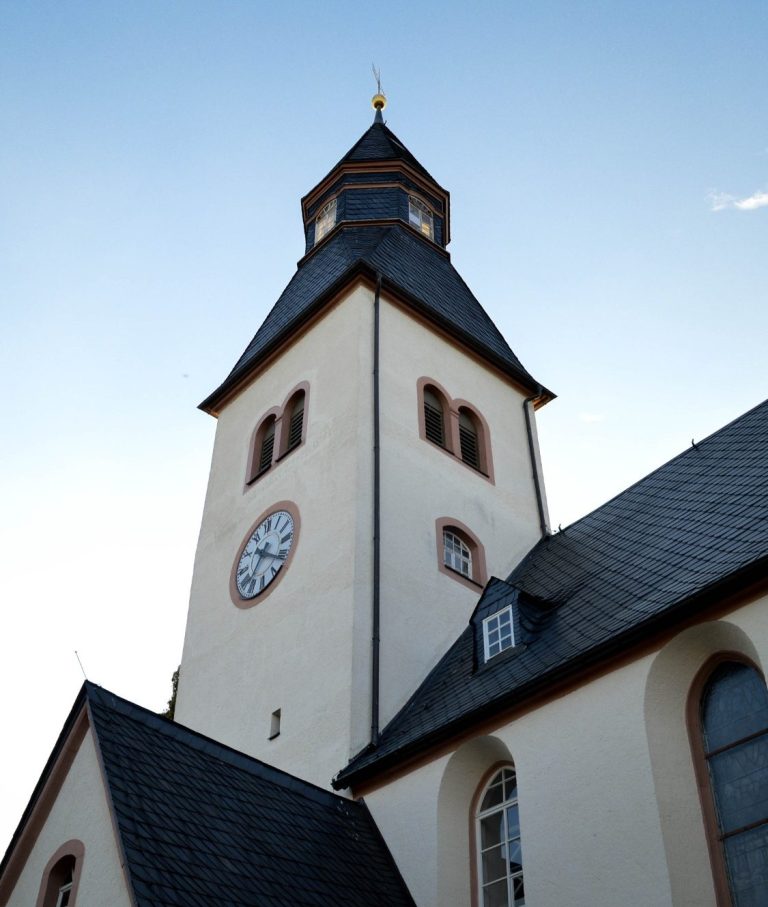 Turm einer Kirche mit Ziffernblatt und goldener Spitze vor klarem Himmel.