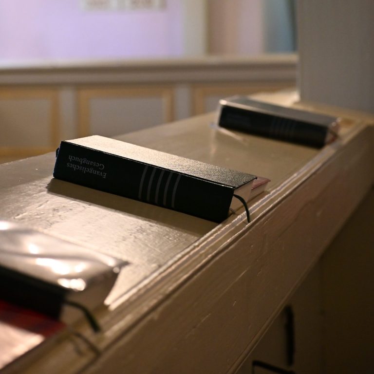 Drei schwarze Bücher liegen auf einer Holzfläche in einem hellen Raum.